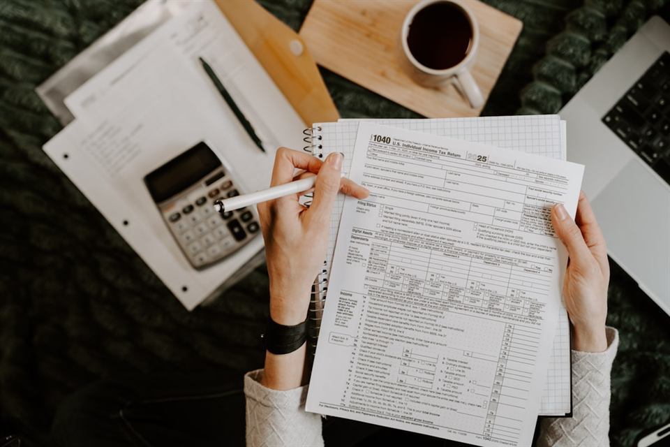 Een persoon vult online financiële gegevens in op een laptop naast papieren jaaroverzichten.